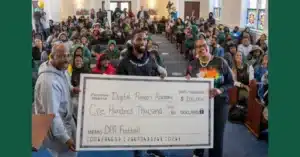 In front of a roomful of students and faculty, members of the Washington Commanders present an oversized check for 100,000 dollars to Digital Pioneers Academy.