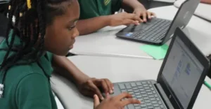 A young black female students works on a laptop at her desk.